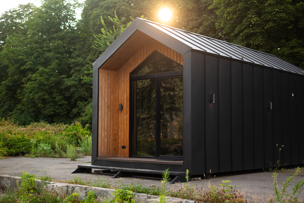 Modern black cabin with wooden doorframe and glass front, set outdoors.