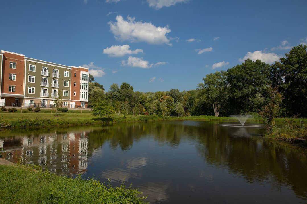 A pond with a fountain in the middle of it and a building in the background.