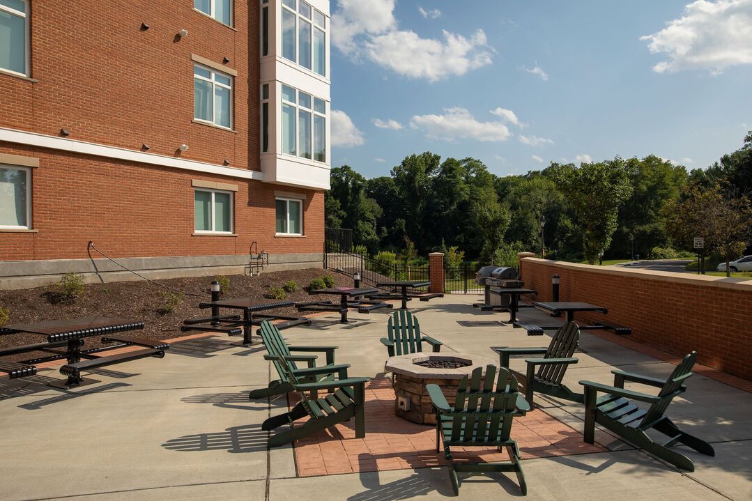 A patio with a fire pit and chairs in front of a brick building.