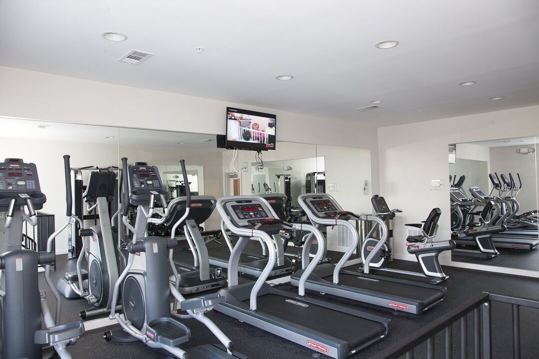 A gym with a lot of treadmills and a tv on the wall.