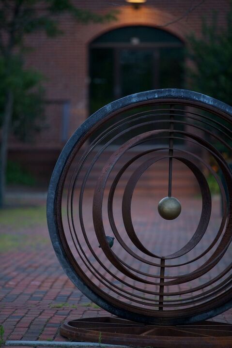 A large metal sculpture is sitting on a brick sidewalk in front of a building.