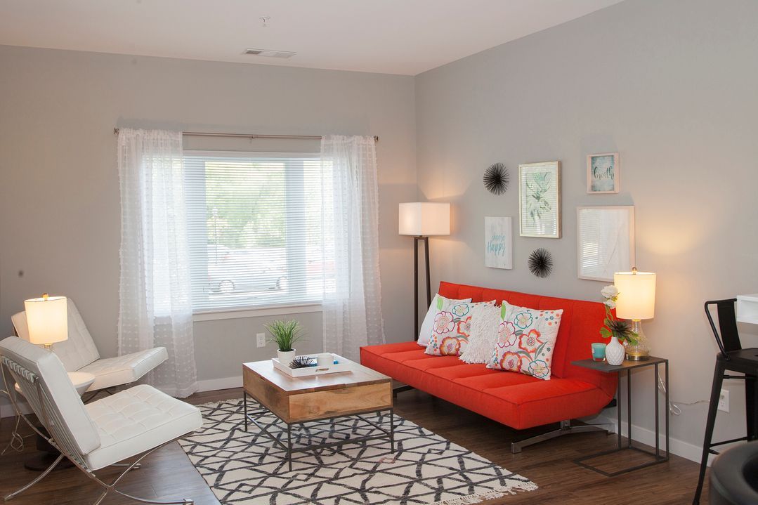 A living room with a red couch , white chairs , a coffee table and a rug.
