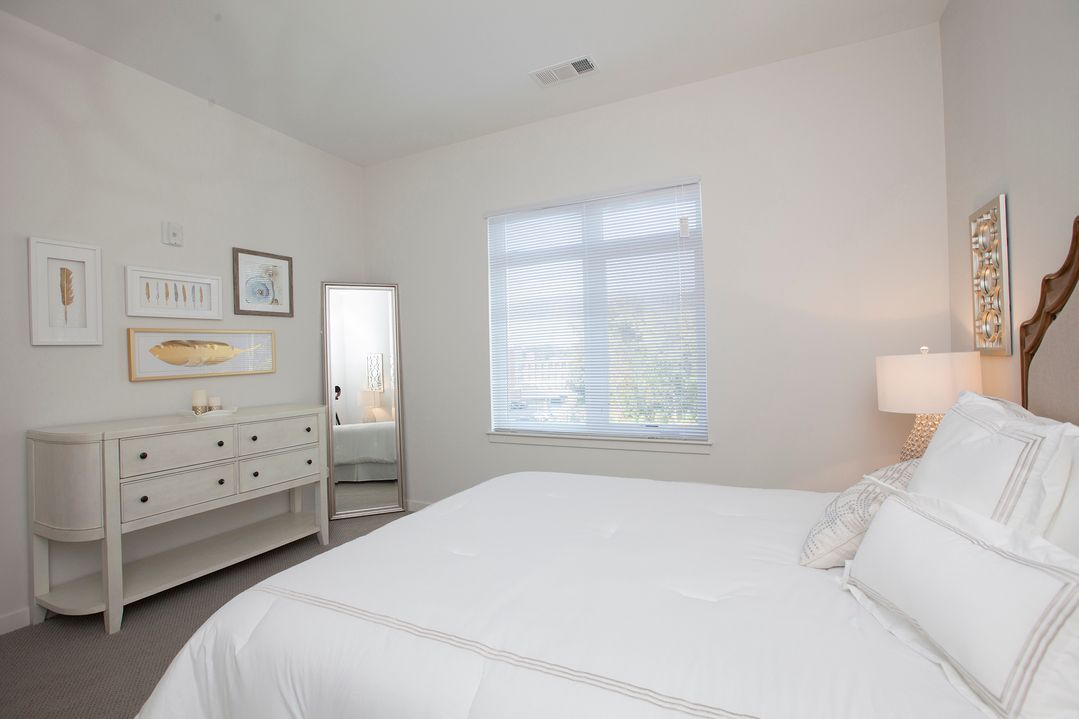 A bedroom with a bed , dresser , mirror and window.