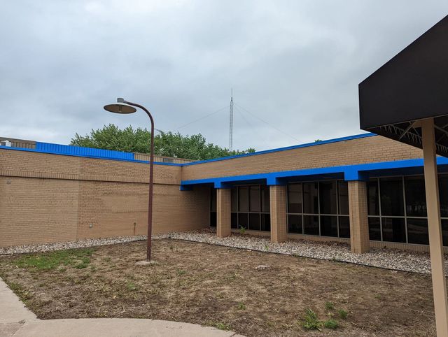 Empty courtyard with a beige building, blue roof trim, and a lamppost under a cloudy sky.