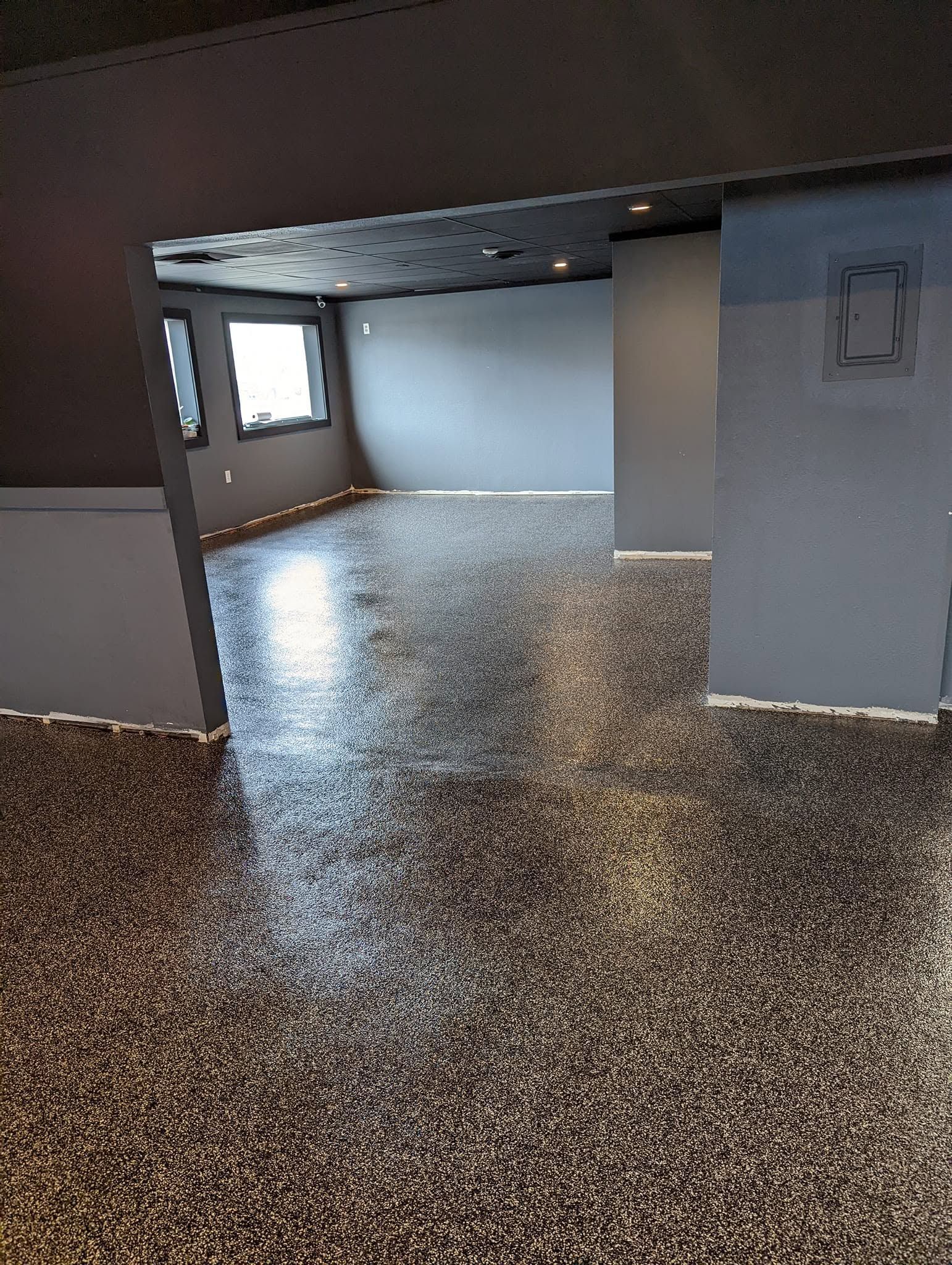 Empty room with terrazzo floor, exposed ceiling, and windows letting in daylight.