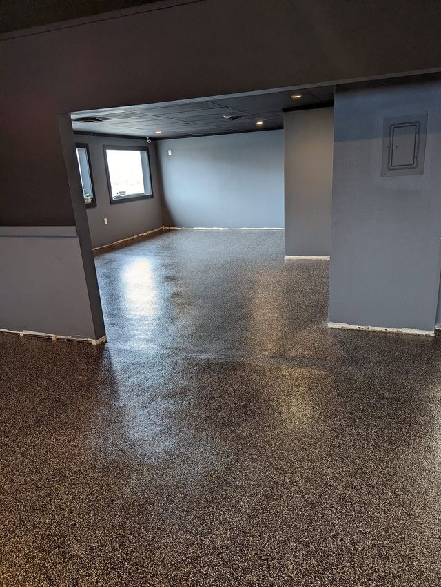 Empty room with terrazzo floor, exposed ceiling, and windows letting in daylight.