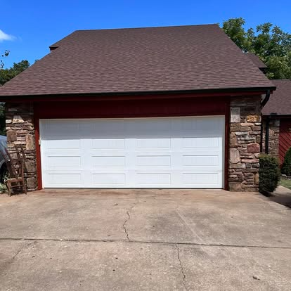 A white garage door is sitting in front of a stone house.