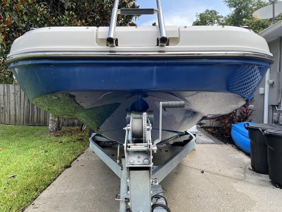 A blue and white boat sits on a trailer in a driveway.