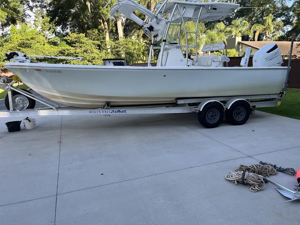 White boat on a trailer in a driveway; trees in background.