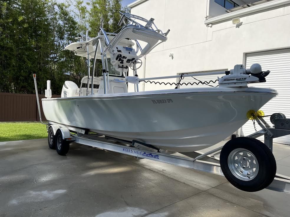 White boat on a trailer, parked in front of a house.