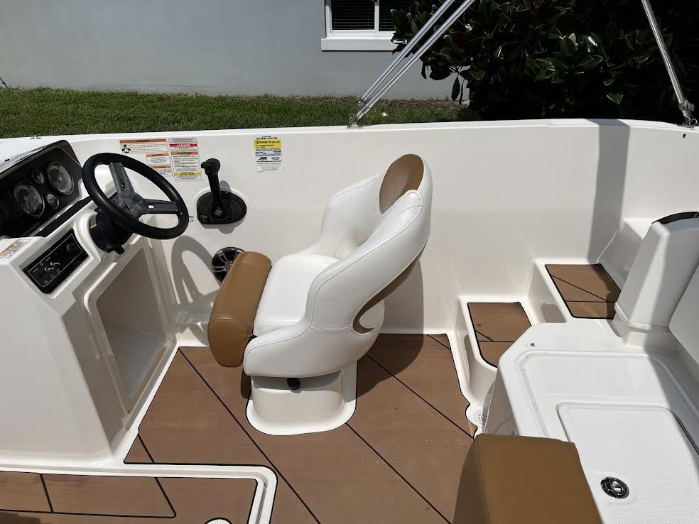 Boat interior with brown and white seat, steering wheel, control panel, and brown flooring.