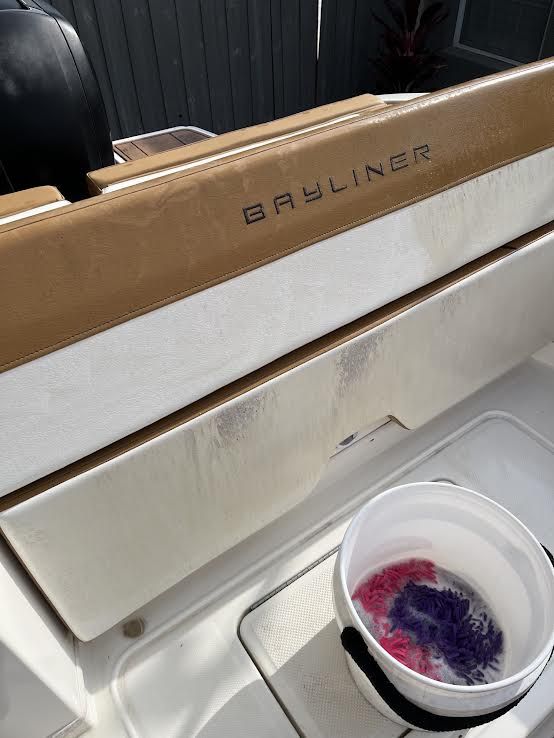 Bayliner boat interior with tan and white seating, a bucket of cleaning supplies.