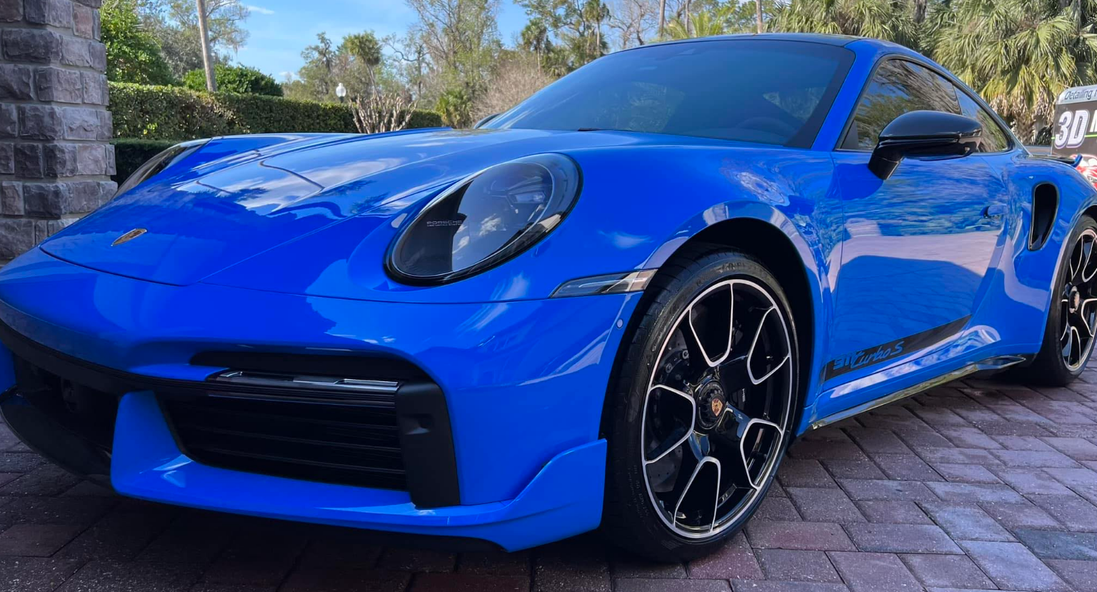 Blue Porsche 911 Turbo S coupe parked in front of a stone building.