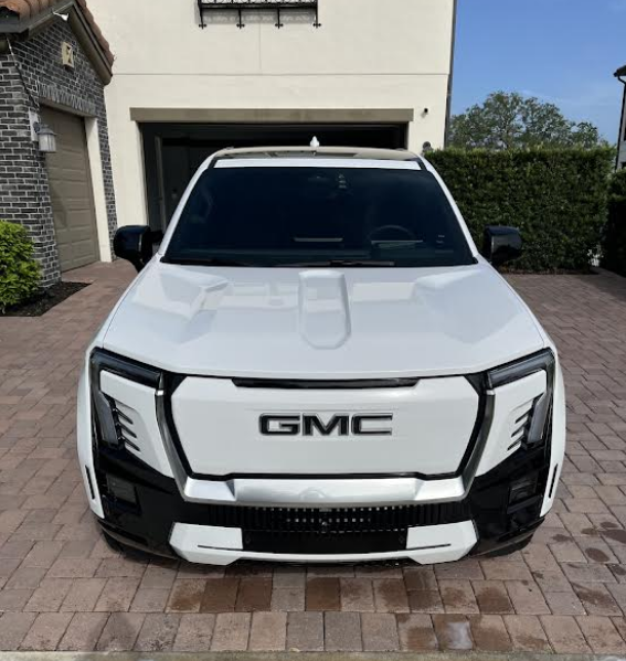 White GMC electric pickup truck parked in front of a house.