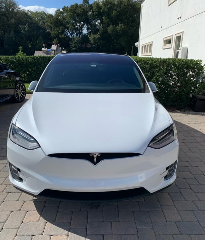 White Tesla Model X electric car parked on a brick driveway in front of a house.