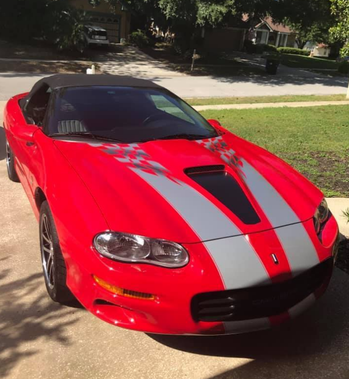 Red convertible car with gray racing stripes parked on a driveway.