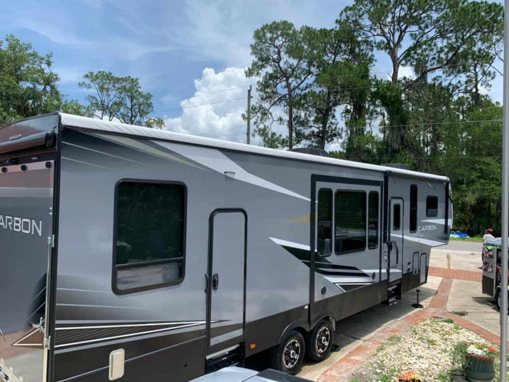Gray and black recreational vehicle parked outdoors under a cloudy sky.