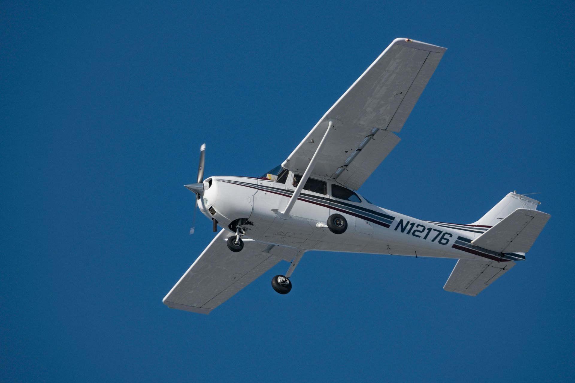 White and blue Cessna airplane in flight against a bright blue sky.