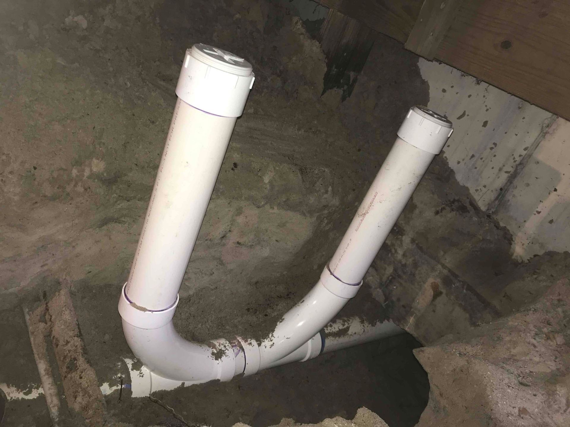 Two white pipes are connected to each other in a hole in the ground.