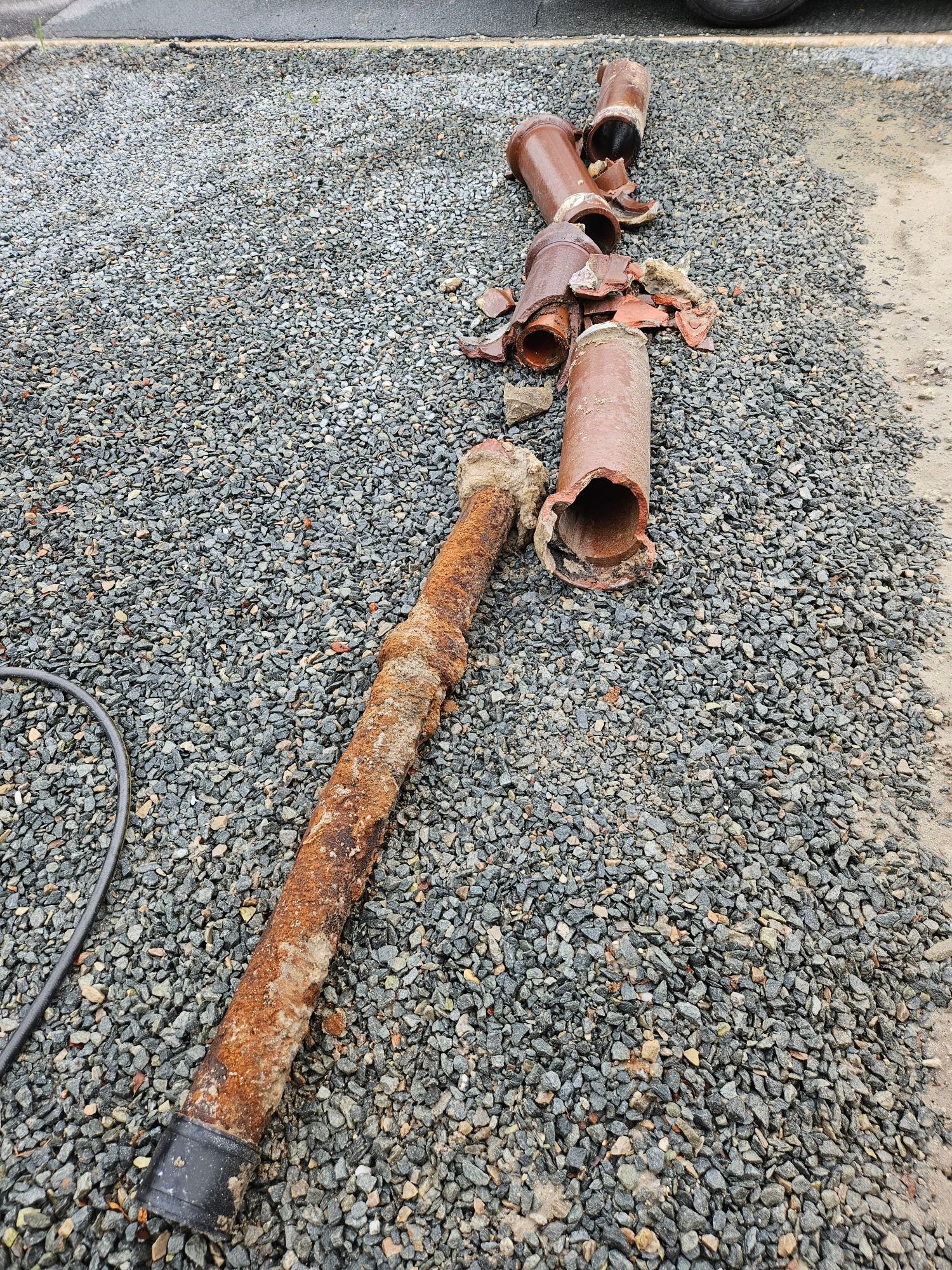 A rusty pipe is laying on a gravel road.