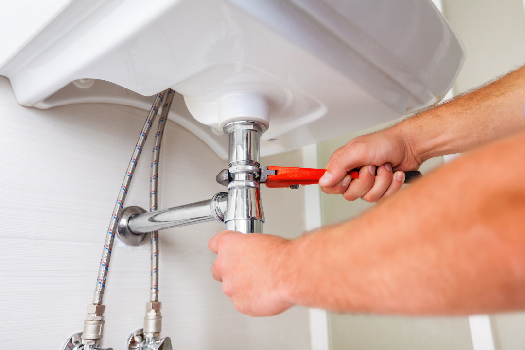 A man is fixing a sink with a wrench.