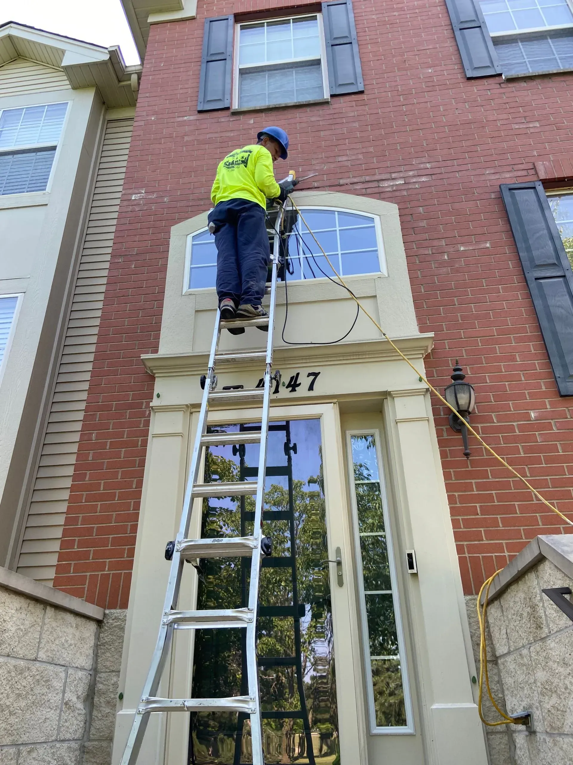 A man is standing on a ladder in front of a brick building.
