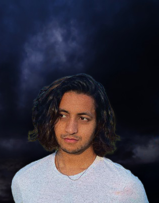 Man with dark hair in a white shirt, looking to the side in a grassy field.