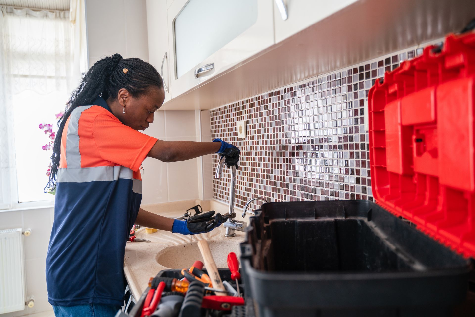 Female Plumber fixing a leak in the kitchen sink of a house.