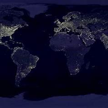 World map at night, showing city lights glowing brightly against the dark oceans and landmasses.