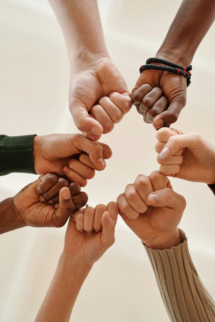 Hands with different skin tones joined in a circle, pinky fingers interlocked in a symbol of unity.