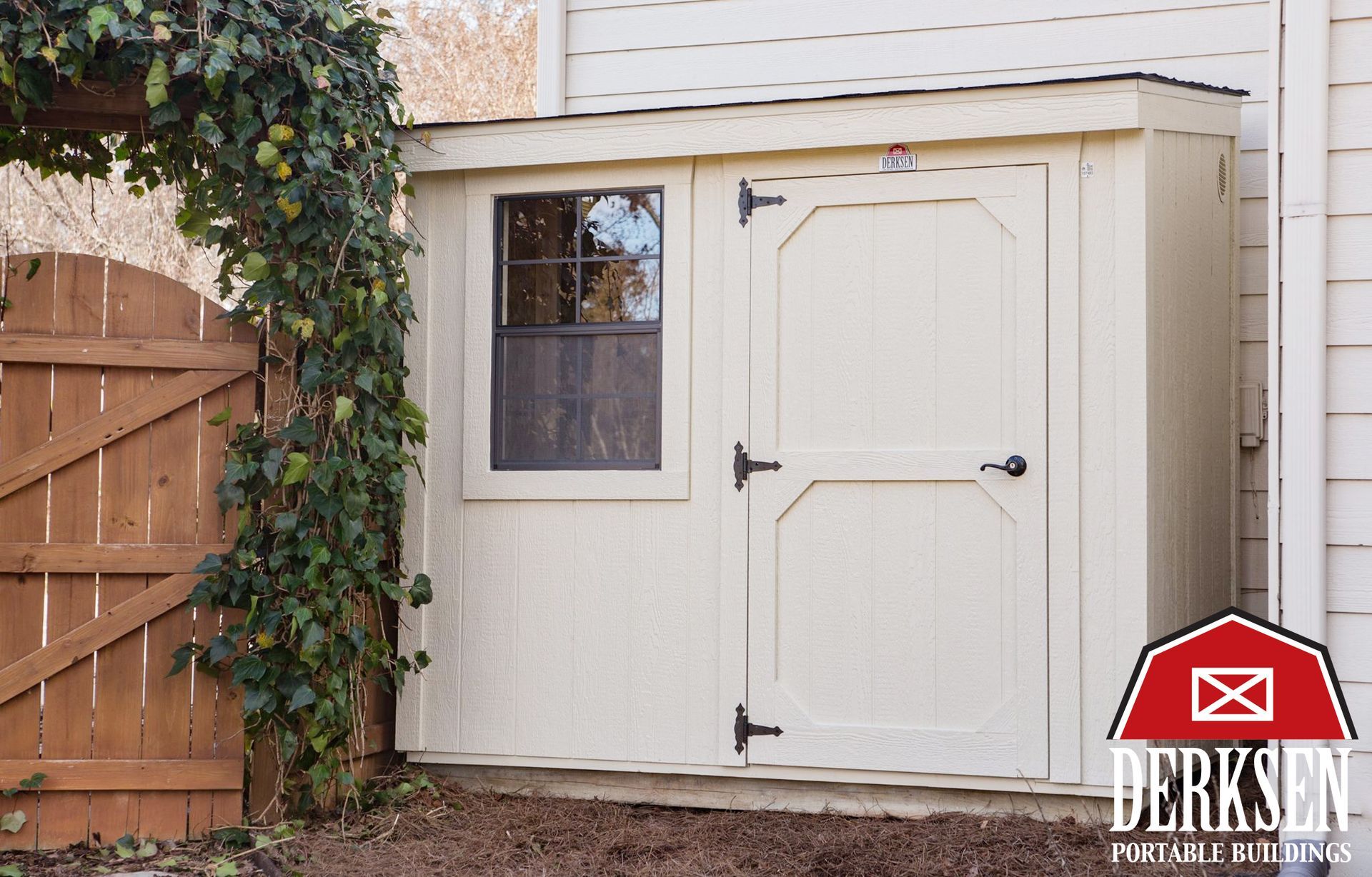 A shed is sitting in the middle of a lush green yard next to a wooden fence.