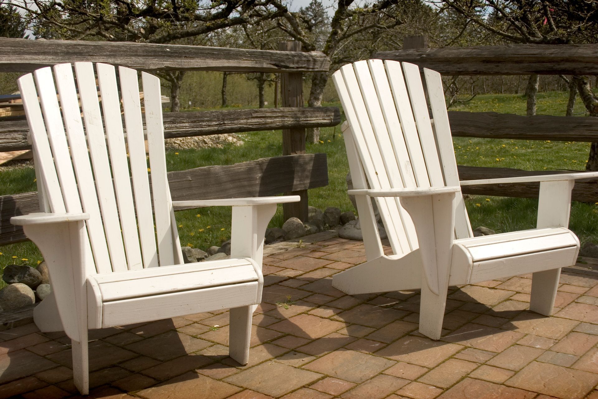 Two white adirondack chairs are sitting on a brick patio