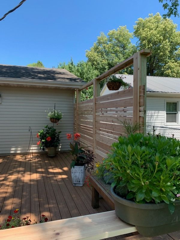 A wooden deck with potted plants and flowers in front of a house.