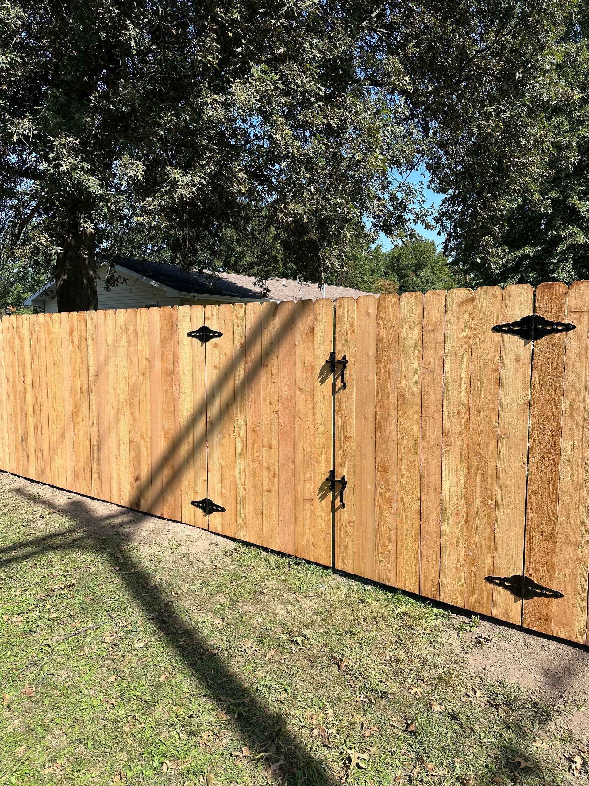 A wooden fence with a gate and a tree in the background.