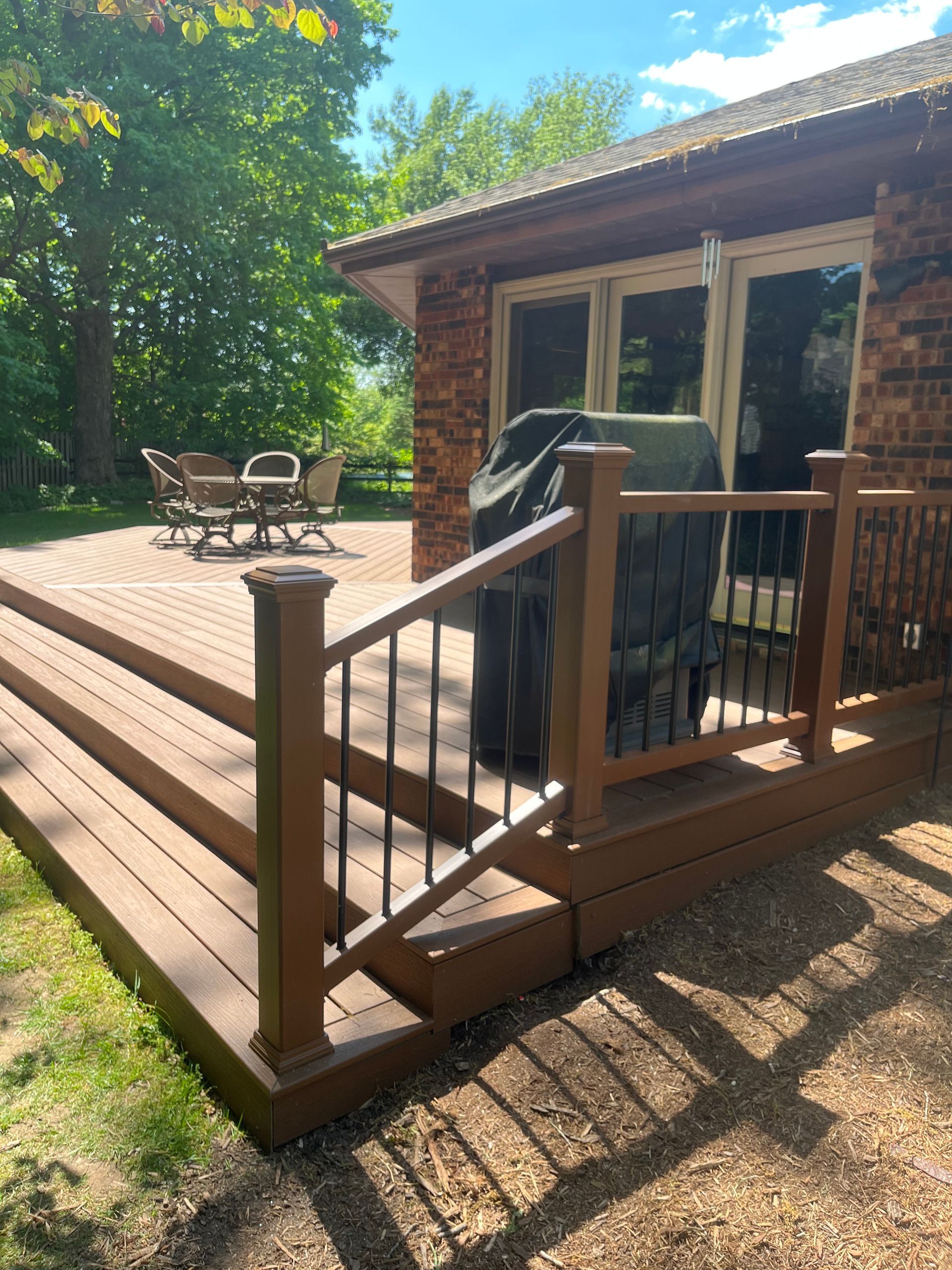 A wooden deck with stairs and a grill in front of a brick house.