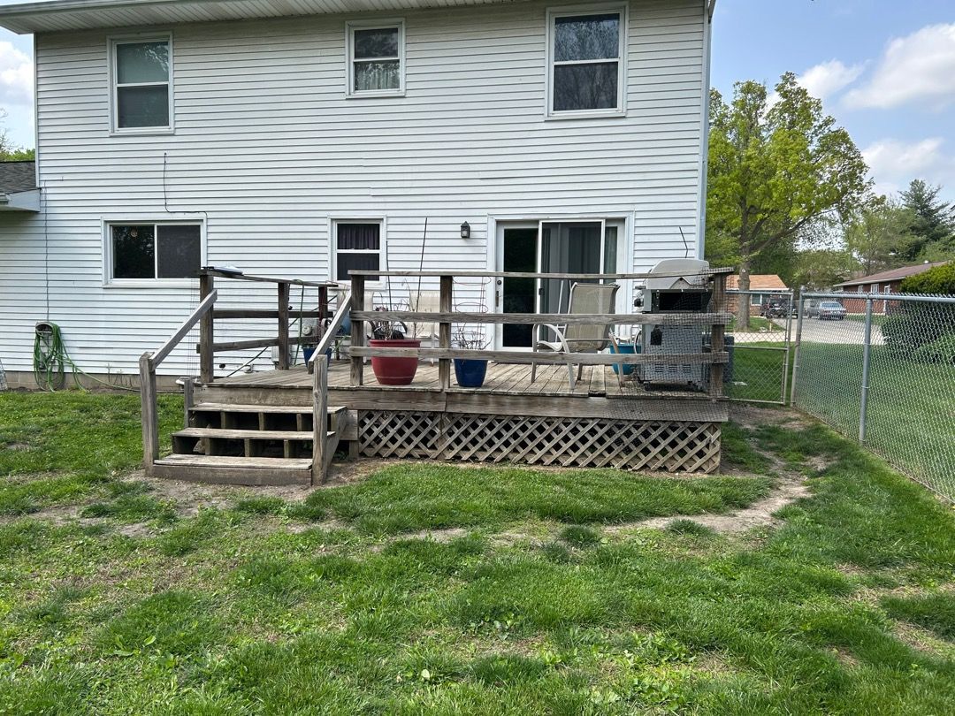 Backyard view of a house with a wooden deck, grill, and a chain link fence.