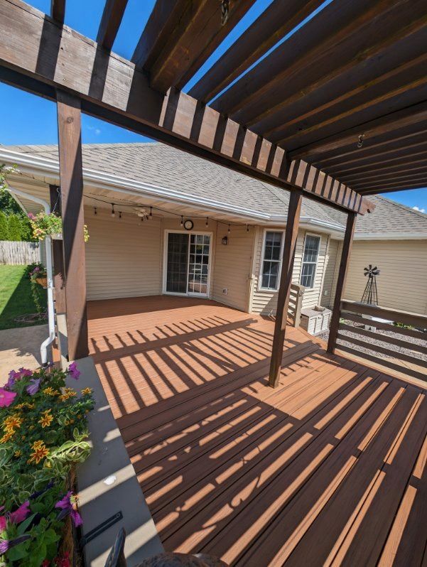 A wooden deck with a pergola and a house in the background
