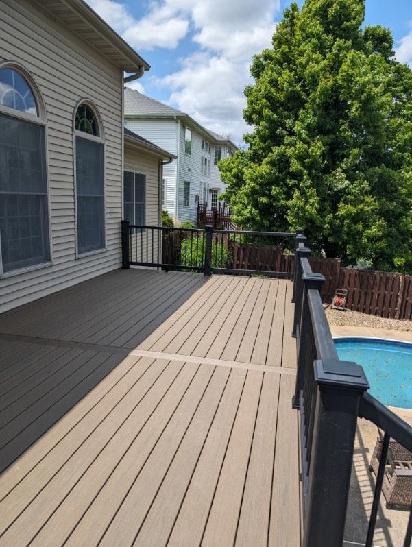 A wooden deck with a black railing next to a swimming pool.