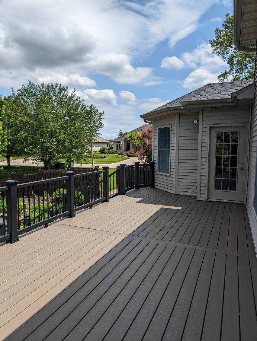 A large deck with a fence and a door in front of a house.