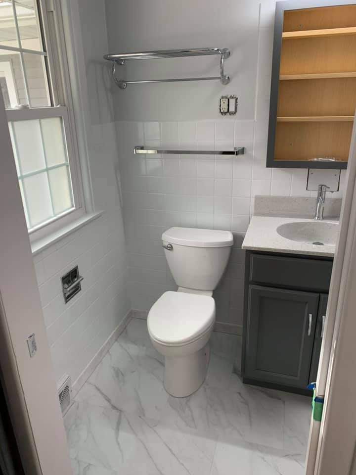 A bathroom with a toilet, sink, mirror and window.