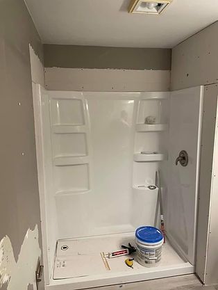 A bathroom with a shower stall and a bucket of paint on the floor.