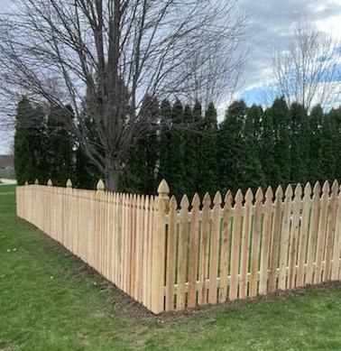 A wooden picket fence is surrounded by trees in a yard.