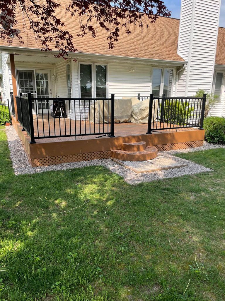 A large deck with a black railing is in front of a house.