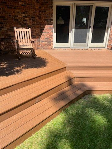 A wooden deck with stairs and a rocking chair in front of a brick house.