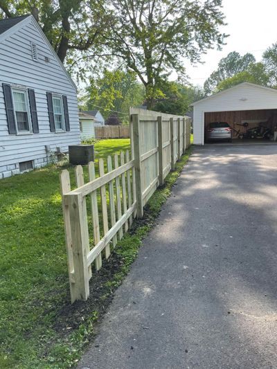 A wooden fence is along the side of a driveway next to a house.