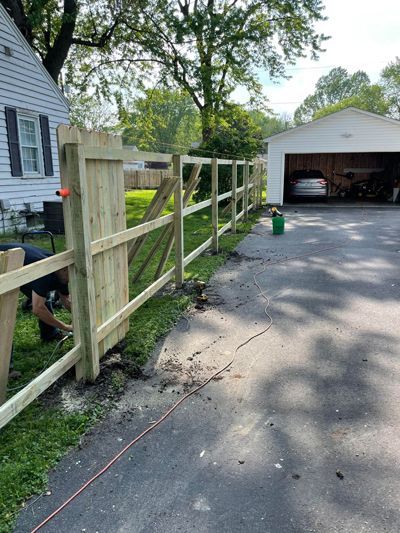 A man is working on a wooden fence in front of a garage.