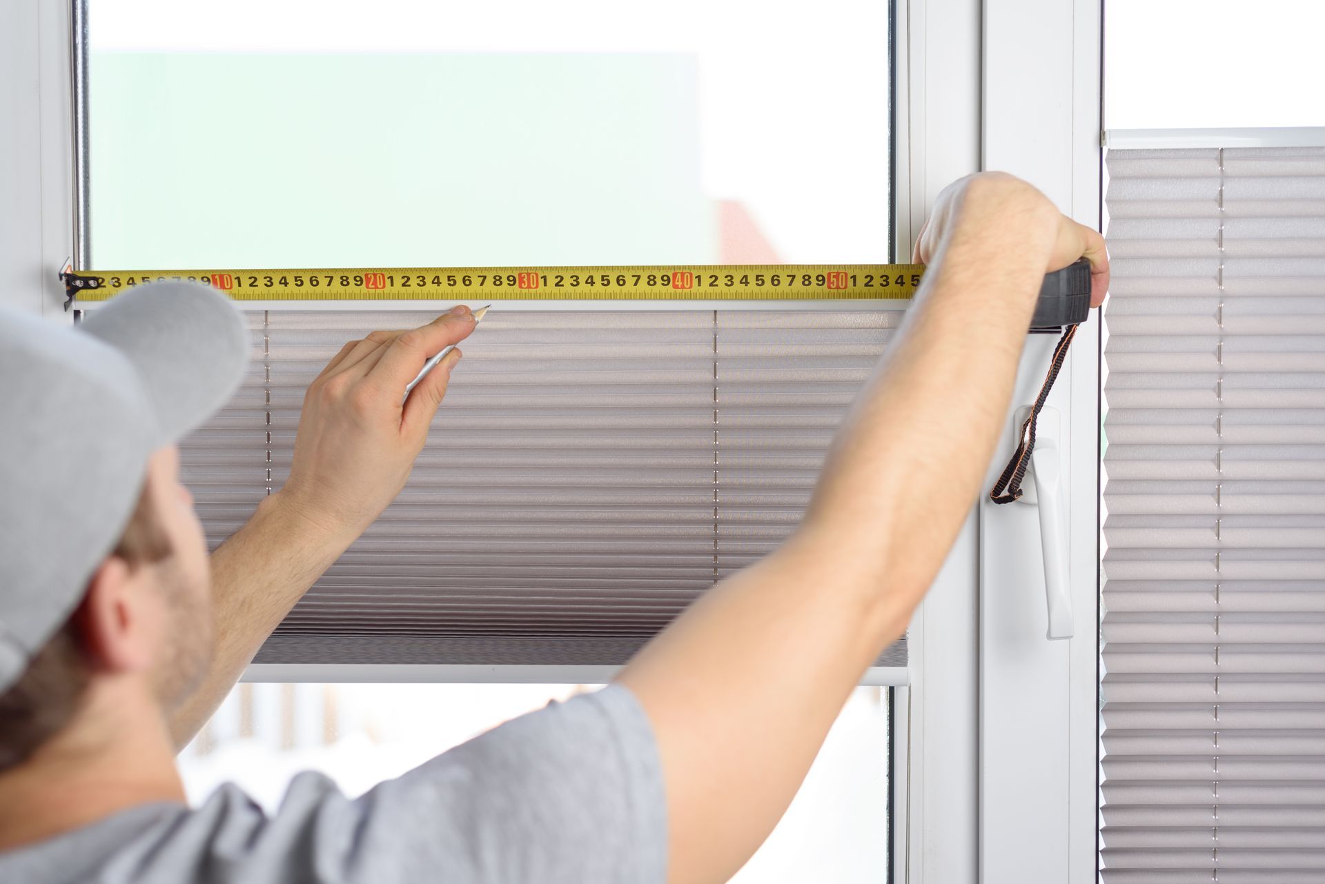 A man installs silver pleated blinds on a window.