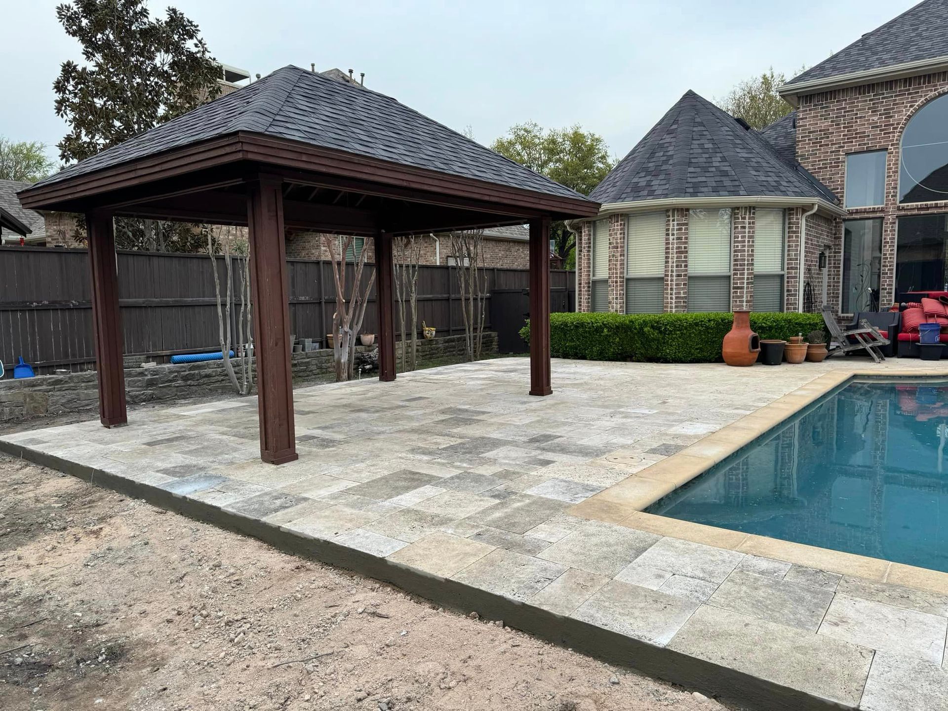 A patio with a gazebo and a pool in the backyard of a house.