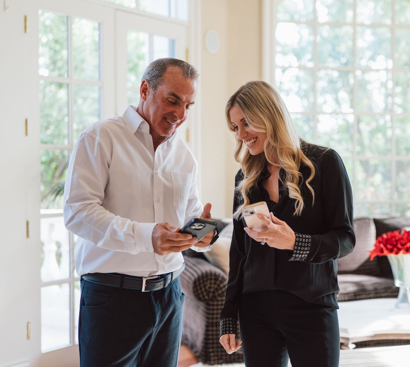 A man and a woman are standing in a living room looking at a tablet.