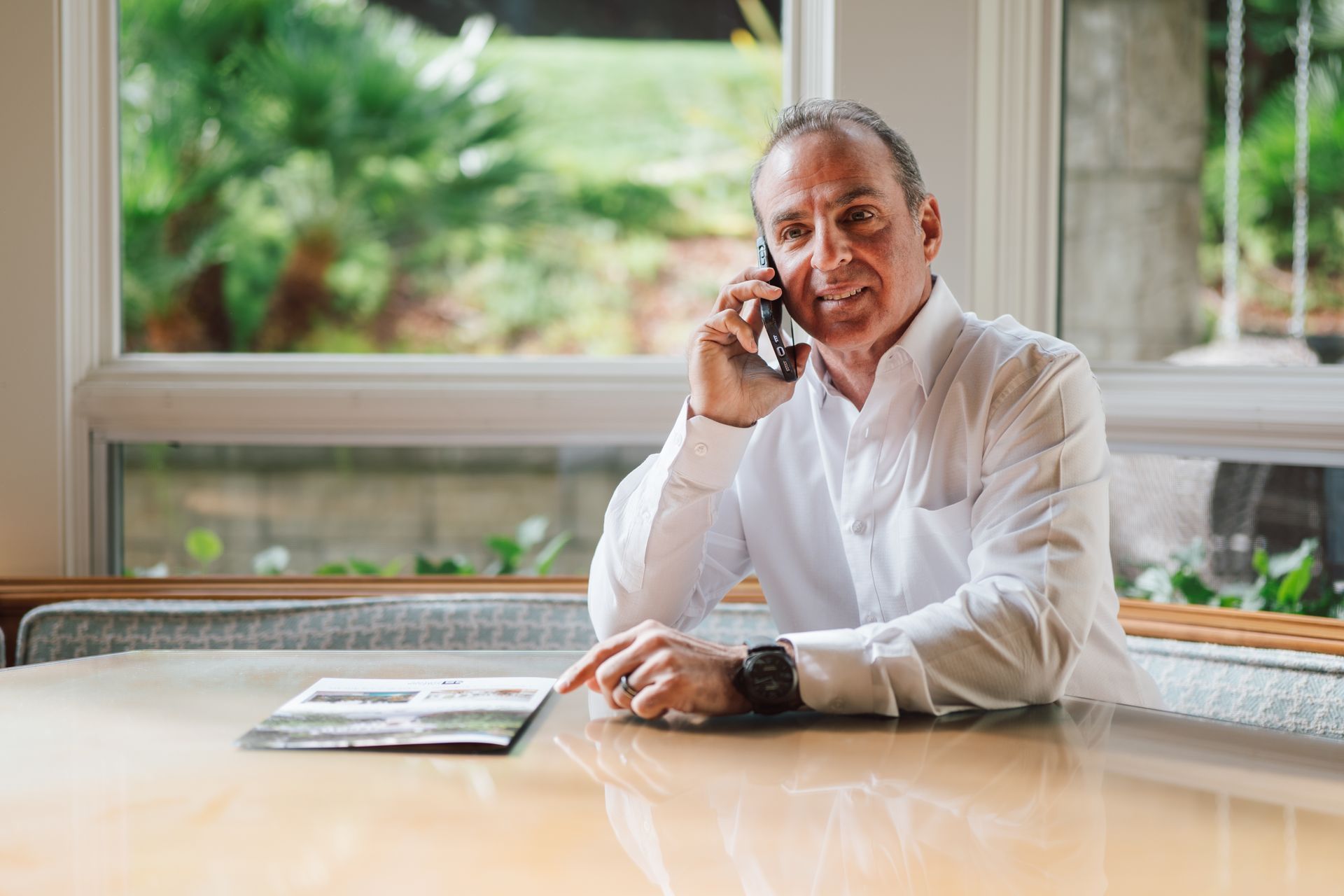 A man is sitting at a table talking on a cell phone.